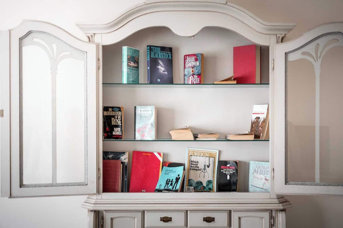 A white, ornate bookcase with multiple shelves containing various books.