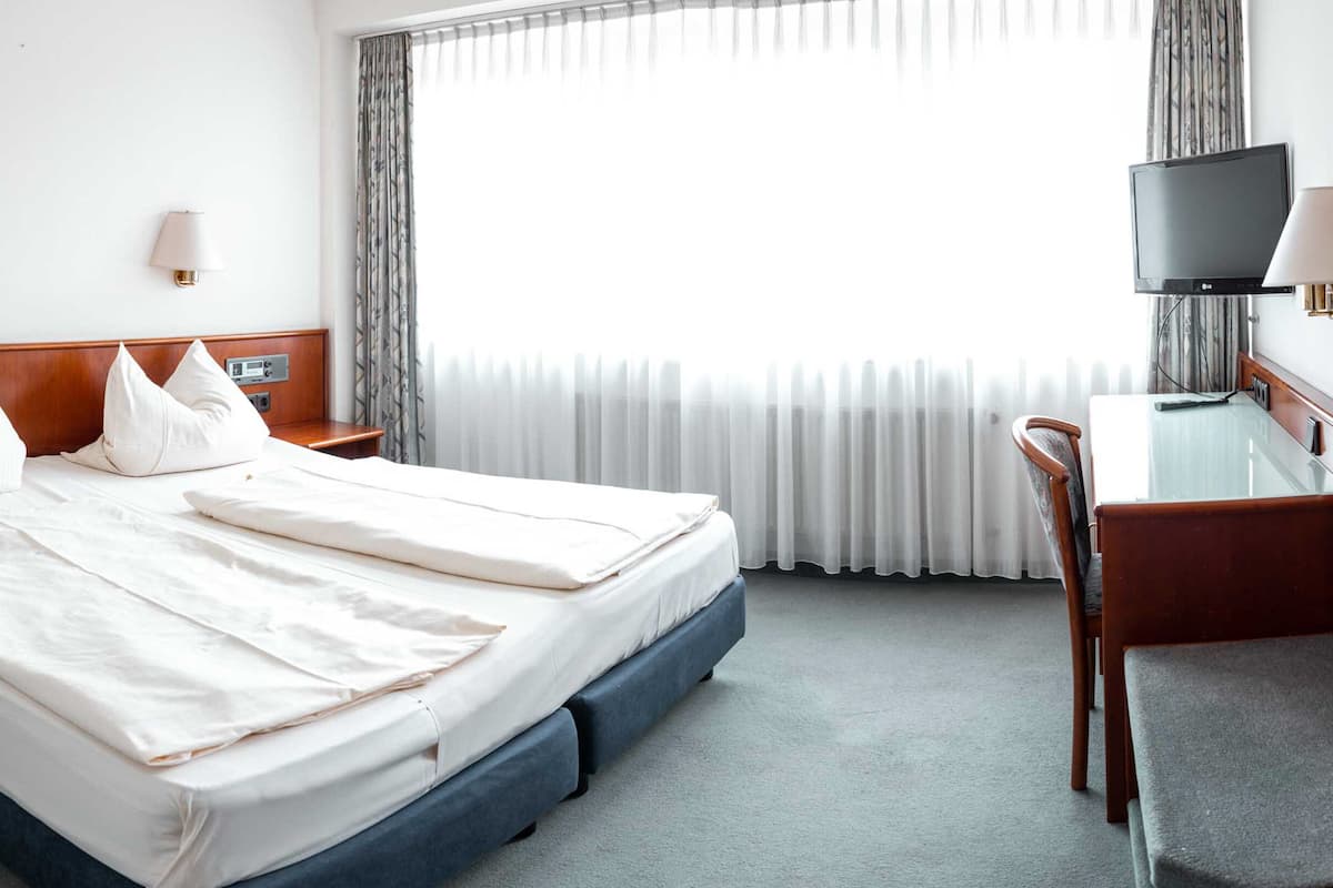 A hotel room with a large bed, a desk, a chair, a TV, and a window with curtains.