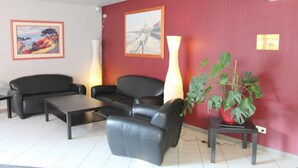 A reception area with a red wall, two black leather sofas, a coffee table, a tall floor lamp, and a potted plant.