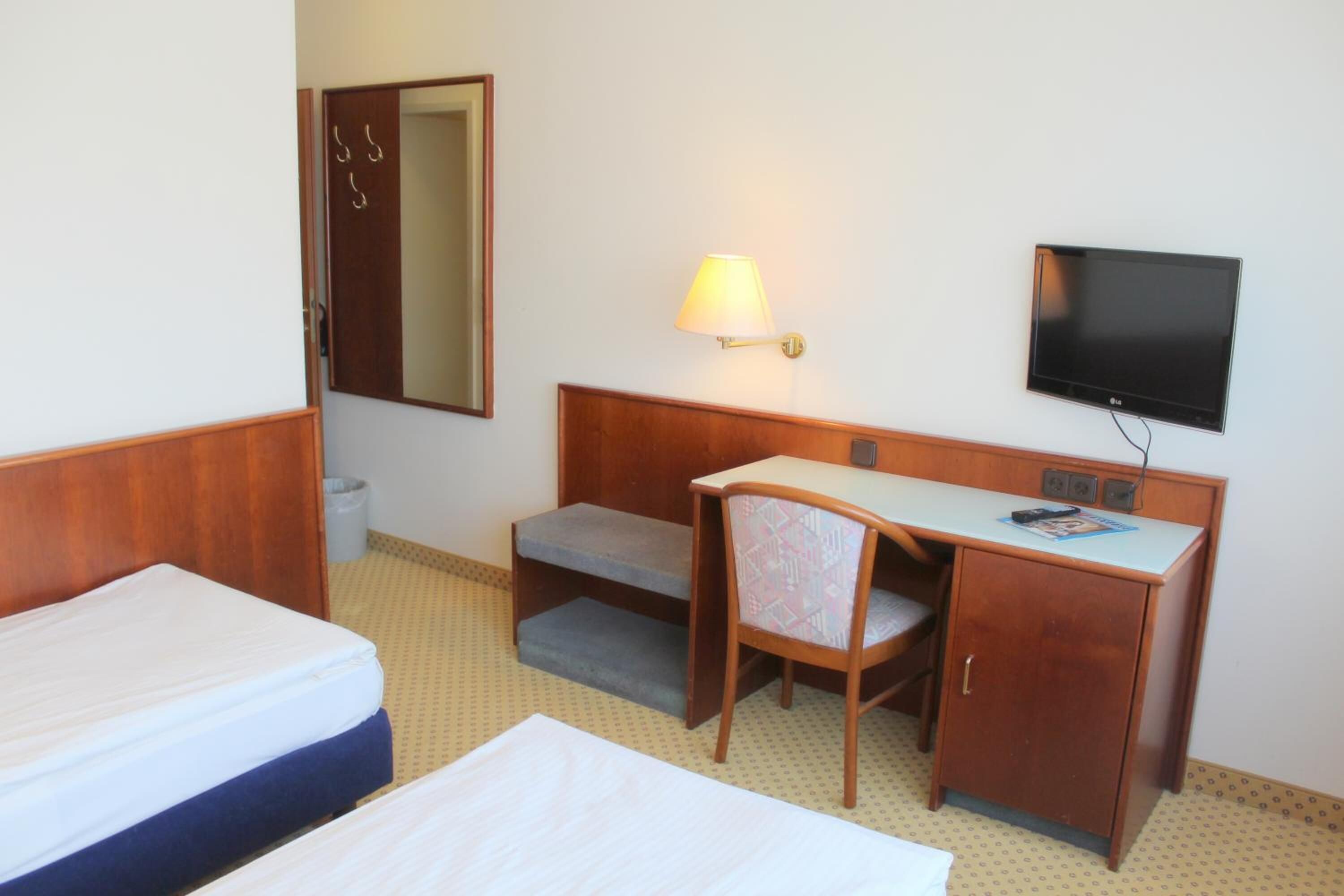 A hotel room with two beds, a desk with a chair, a television, and a lamp.