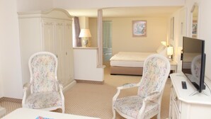 A hotel room with a bed, two armchairs, a television, a desk, and a wardrobe.