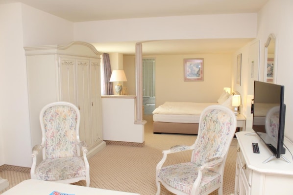A hotel room with a bed, two armchairs, a television, a desk, and a wardrobe.