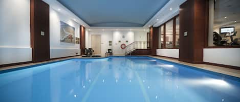 Una amplia piscina interior con suelo azul, rodeada de paredes con paneles de madera y una barandilla de cristal.