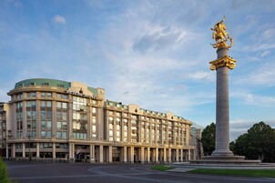 Un edificio grande de varios pisos con estilo arquitectónico clásico, que presenta una columna central con una estatua dorada.