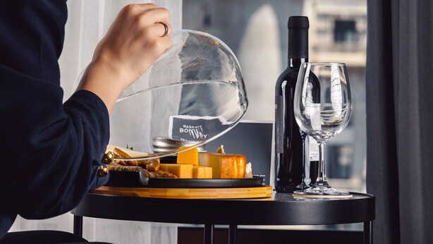 Una persona sentada a una mesa con una botella de vino, una copa y un plato de queso.