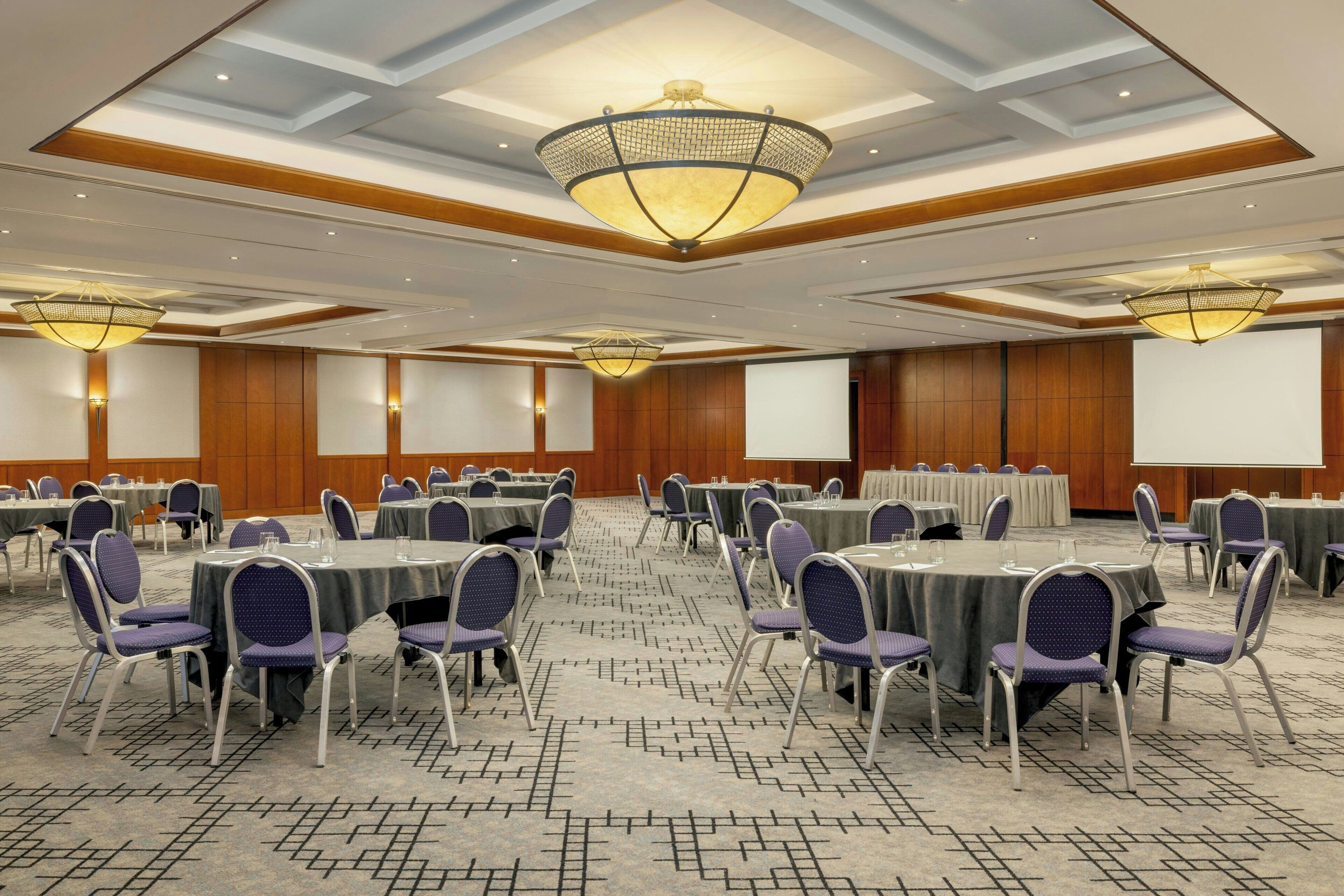 A conference room with round tables, chairs, and a large screen.