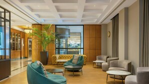 Un hall moderno con piso de madera, una planta grande en maceta, un sofá amarillo y varios sillones grises.