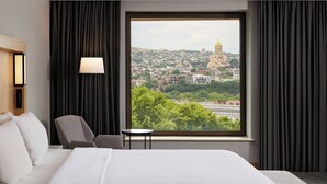 Habitación de hotel con un ventanal grande, una cama, una silla y una mesita.