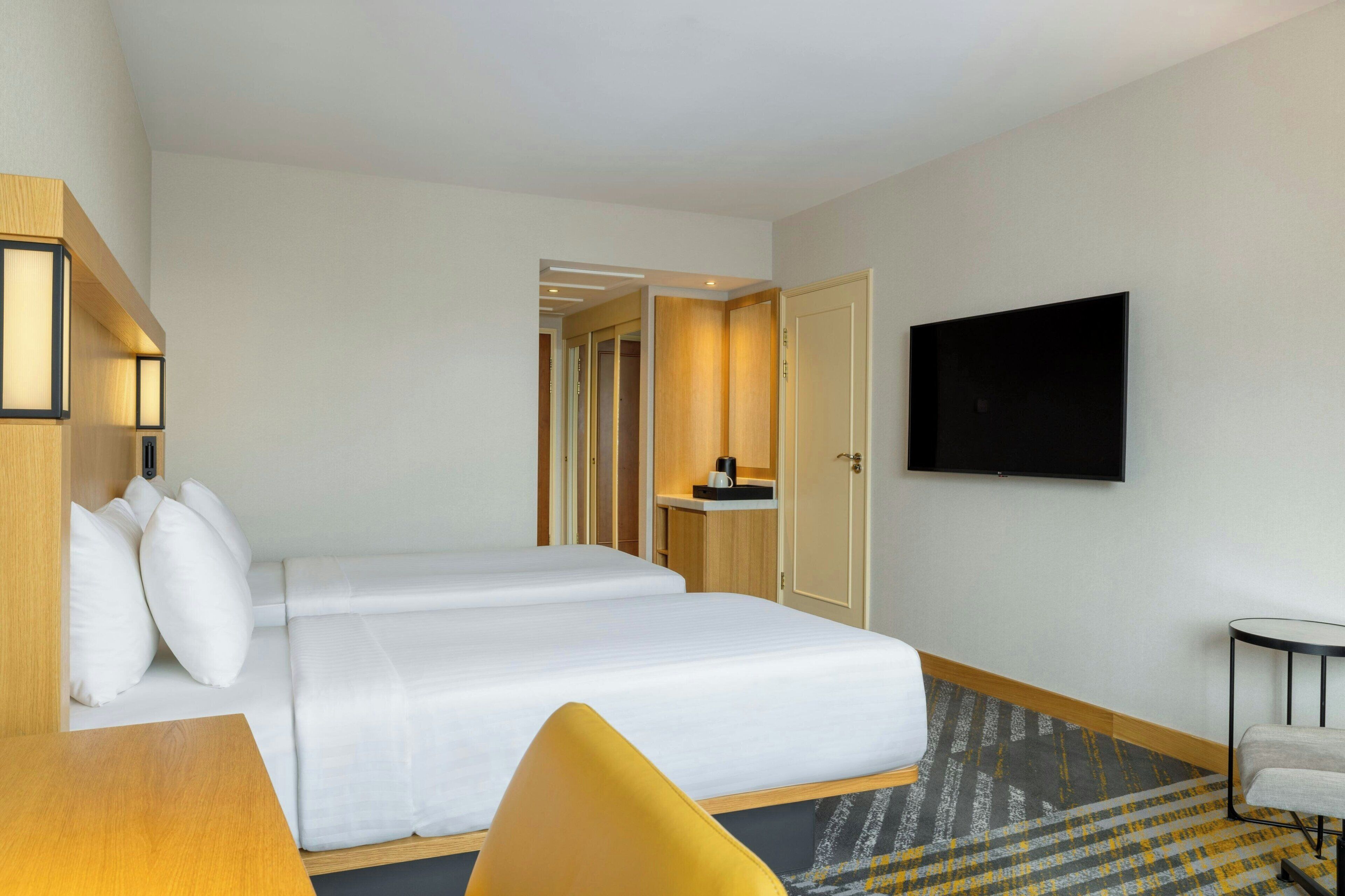 A hotel room with a bed, a desk, a chair, a television, and a bathroom visible through an open door.
