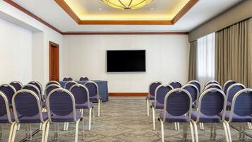 Un salón de conferencias con filas de sillas, un televisor de pantalla plana grande y una alfombra estampada.