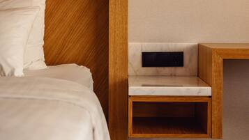 Una habitación de hotel moderna con un cabecero de madera, una mesita de noche con lámpara integrada y una pequeña mesita auxiliar de madera.