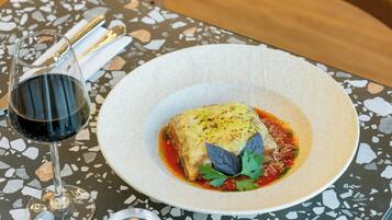 Prato de comida com um copo de vinho tinto sobre uma mesa com superfície de terrazzo.