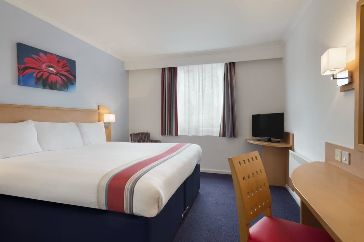 A hotel room with a large bed, a desk with a television, and a chair.