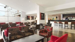 A modern hotel lobby with seating areas, a bar, and a visible staircase. - Ramada by Wyndham Wakefield (Ossett)