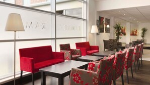 A modern hotel lobby with red seating, a large window, and a wall with the name 'RAMADA'. - Ramada by Wyndham Wakefield (Ossett)