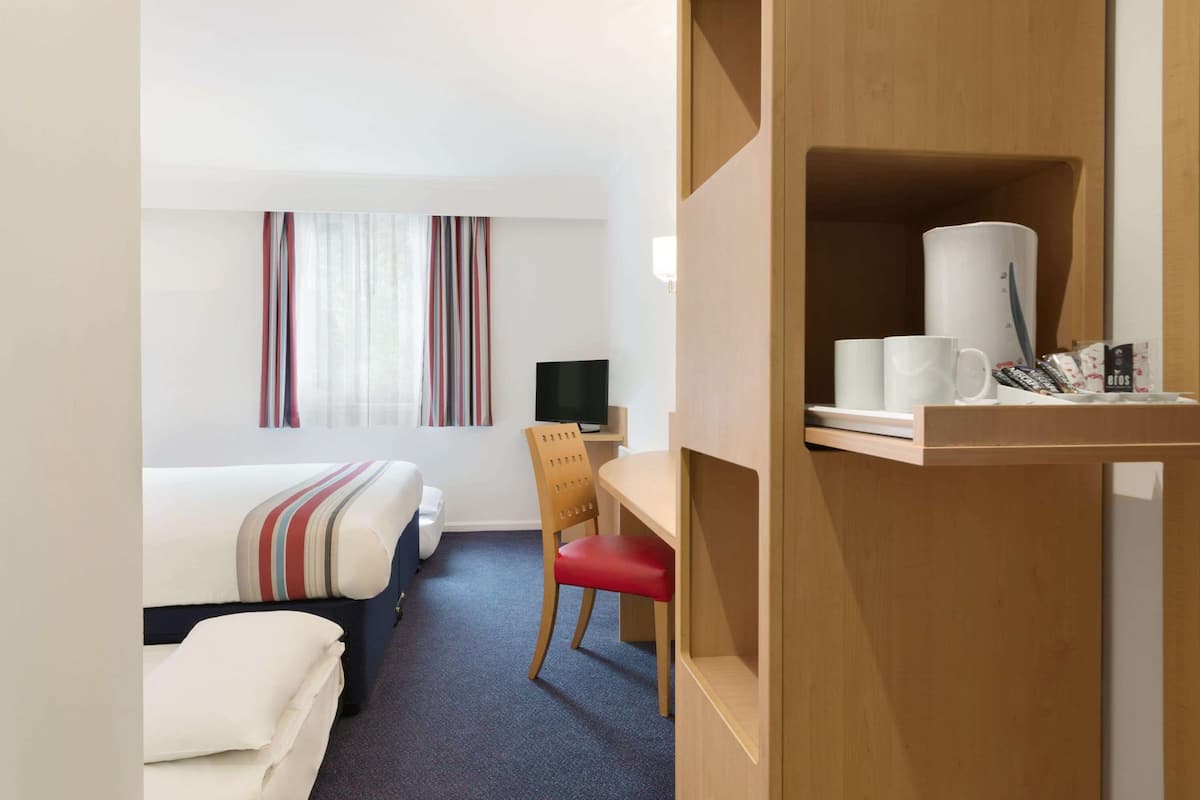 A hotel room with a bed, a desk with a chair, a television, and a shelf with toiletries.