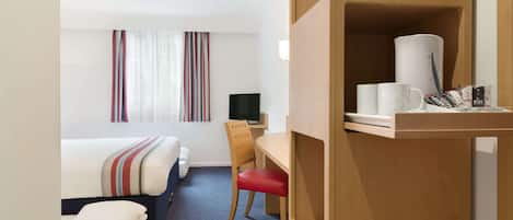 A hotel room with a bed, a desk with a chair, a television, and a shelf with toiletries.