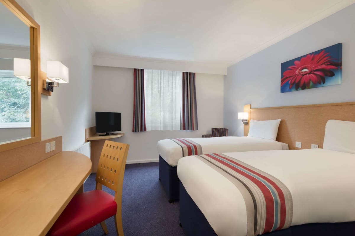 A hotel room with two beds, a desk, a chair, a TV, and a window with curtains.