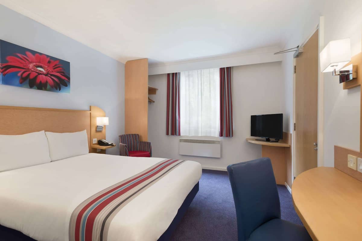 A hotel room with a large bed, a desk, a chair, a television, and a window with curtains.