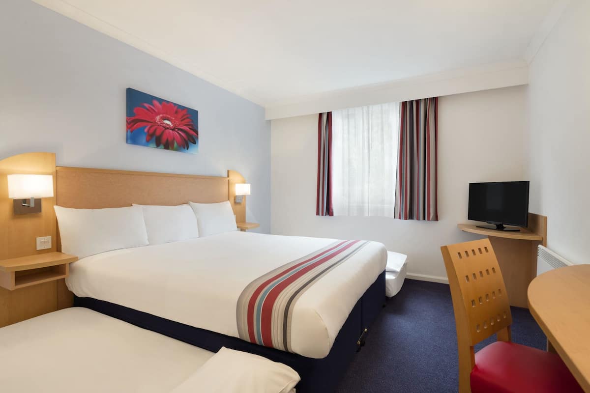 A hotel room with a large bed, a television, a desk, and a chair.