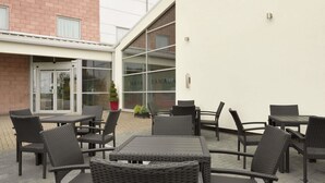 An outdoor patio area with wicker furniture and a glass door entrance. - Ramada by Wyndham Wakefield (Ossett)