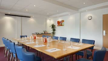 A conference room with a long table, blue chairs, and a clock on the wall.