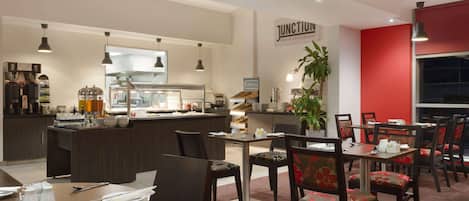 Ein Restaurant mit Barbereich, Esstischen, Stühlen und einer Küche im Hintergrund.