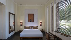 A hotel room with a large bed, two bedside tables, a desk with a chair, and a window with blinds.
