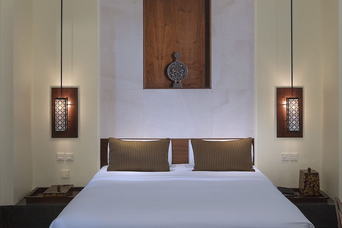 A large bed with a wooden headboard, two wall-mounted sconces, and a decorative wall piece above the bed.