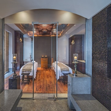A modern hotel room with two beds, a wooden floor, and a glass partition.