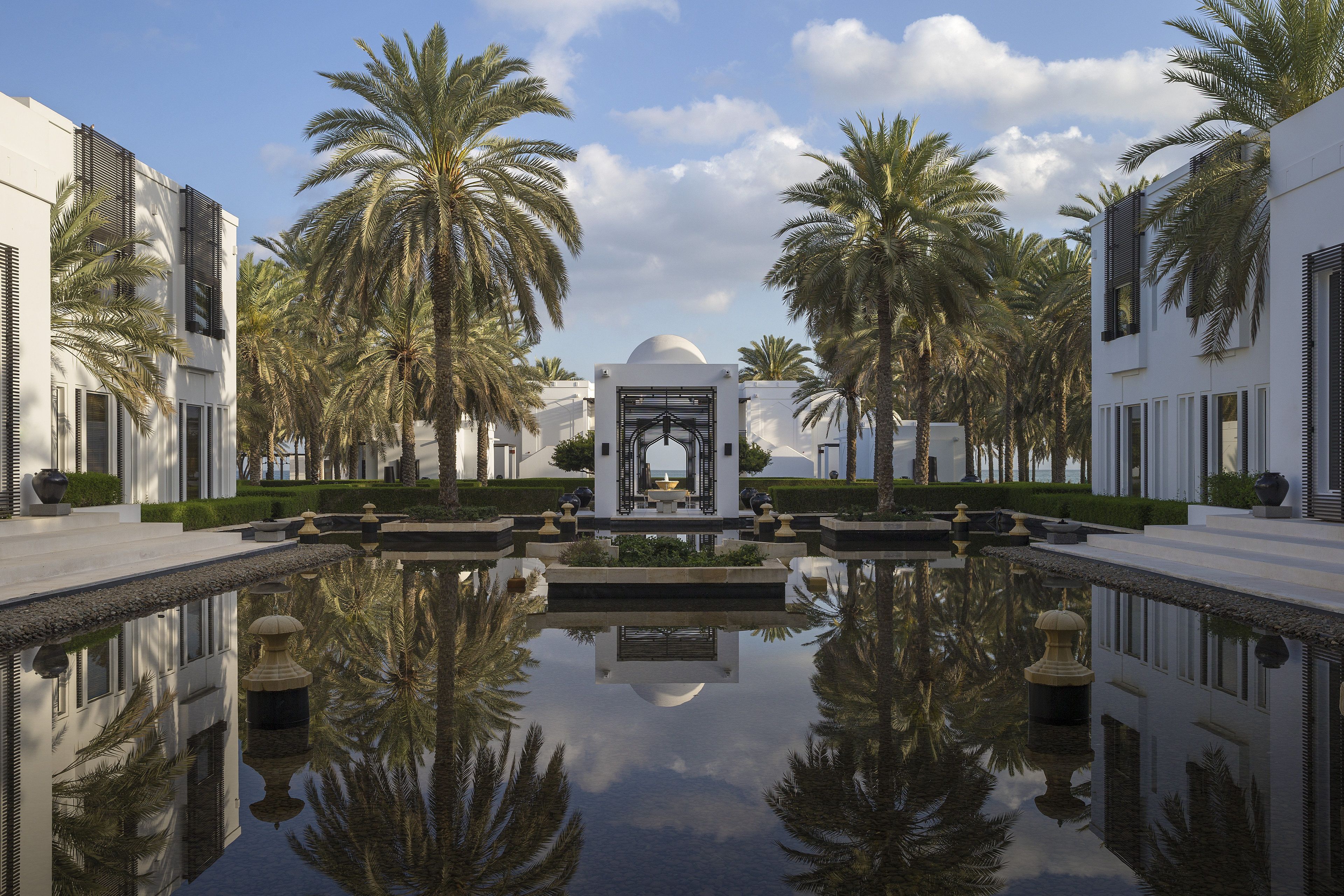 Una piscina simétrica con palmeras y una fuente central, rodeada de edificios modernos.