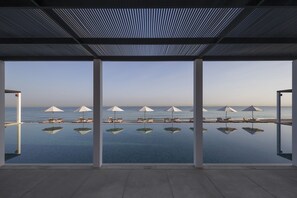 An infinity pool with clear reflections, white umbrellas, and lounge chairs facing the ocean. - The Chedi Muscat (Muscat)