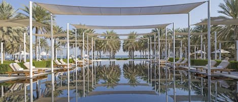 A pool area with sun loungers and umbrellas, surrounded by palm trees.