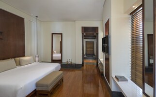 Una habitación de hotel con una cama grande, un banco, un televisor y un espejo.
