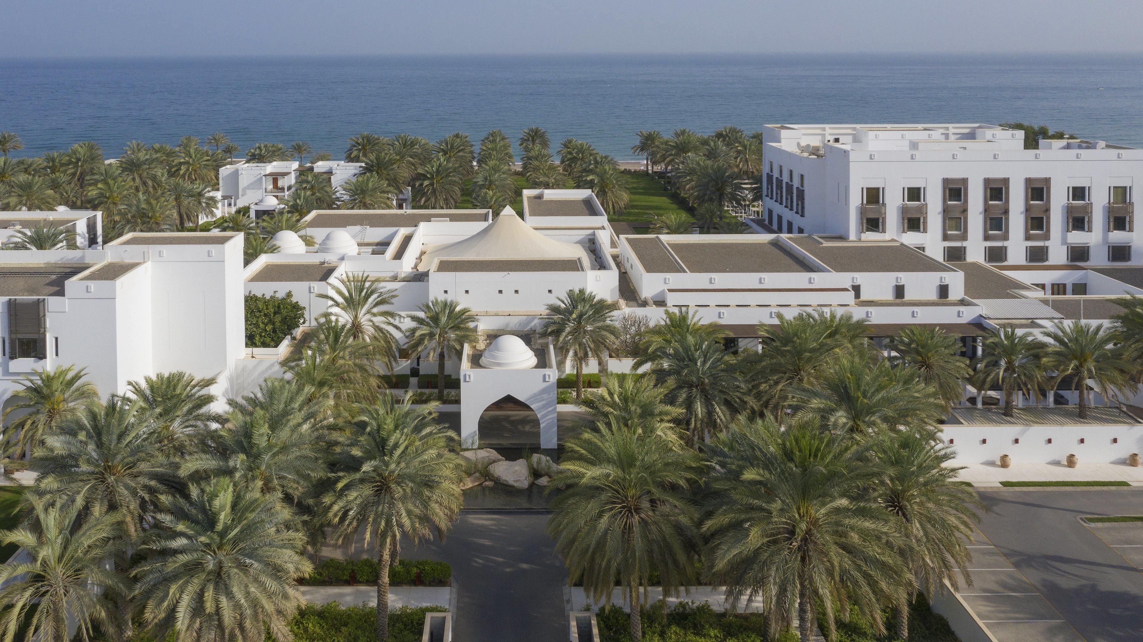 A modern building with a central dome and surrounding palm trees, overlooking a body of water.