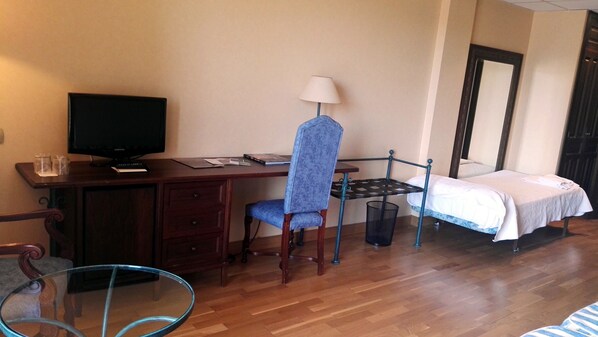 A hotel room with a wooden desk, a chair, a bed with a white bedspread, a television, and a small table with a lamp. - Hotel Spa Tudanca Aranda (Fuentespina)