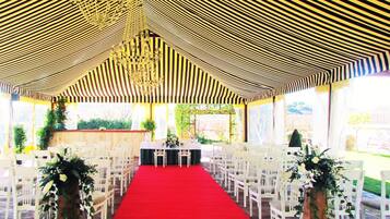 Un espacio para eventos con carpas, una alfombra roja, sillas blancas y decoración floral.