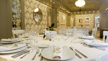 A banquet table set with white tablecloths, silverware, and wine glasses, indicating a formal dining arrangement.