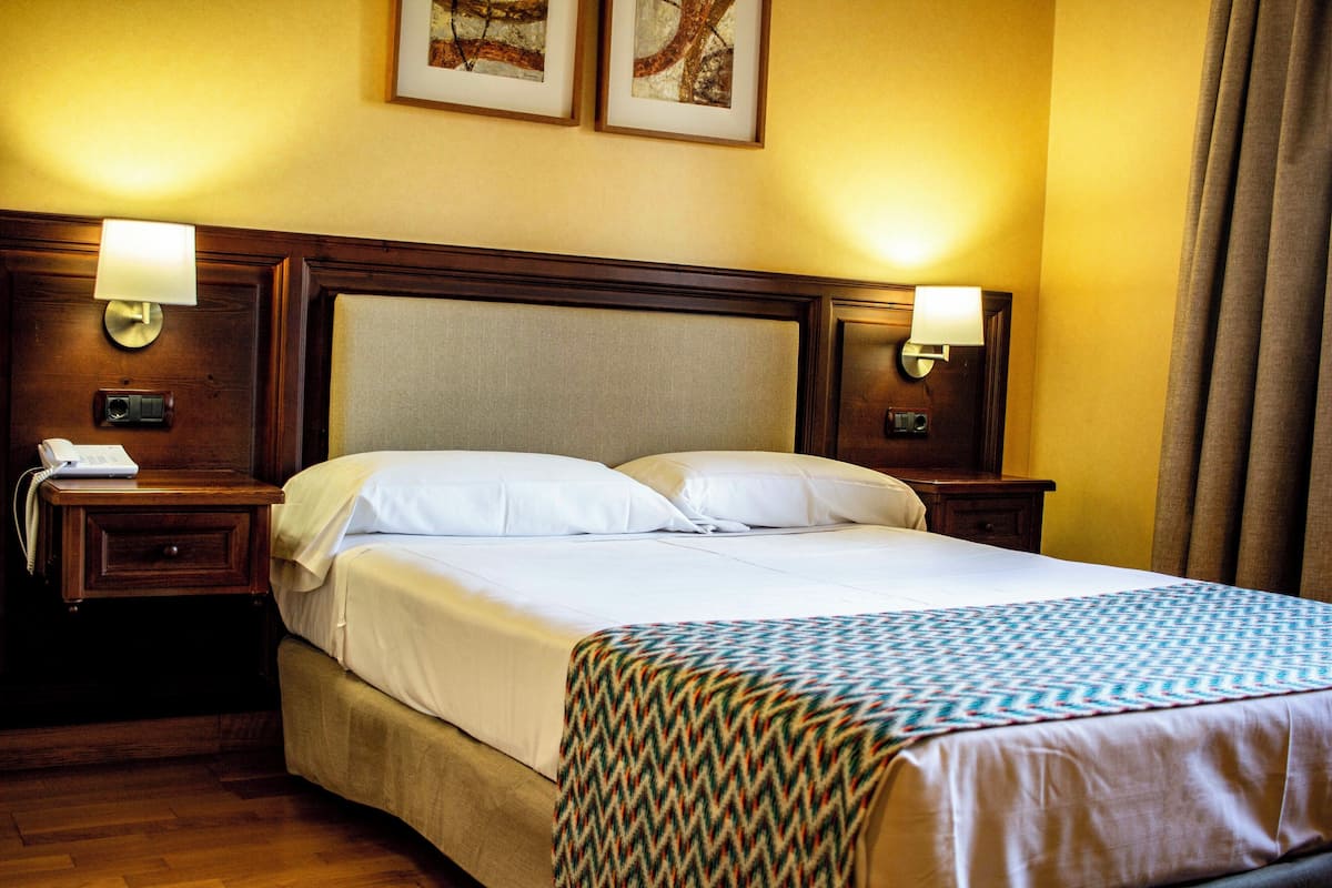 Une chambre d’hôtel avec un grand lit, deux tables de chevet, une petite table et une lampe.