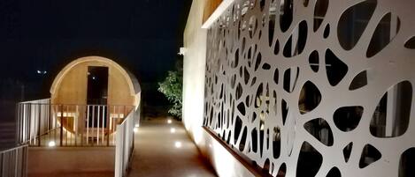 Un pasillo con una puerta de madera al final, una pared decorativa blanca con diseños recortados y una barandilla a la izquierda.