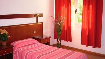 Une chambre d’hôtel avec une tête de lit en bois, deux lits avec une literie à rayures, une table de chevet, un vase avec des fleurs et des rideaux rouges.