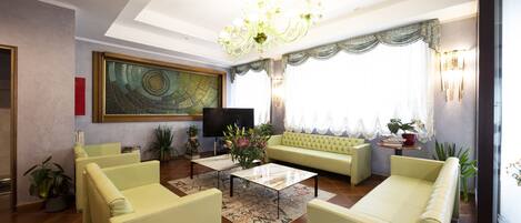 A spacious living room with a large painting, a chandelier, and a sofa set.