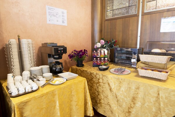 A breakfast buffet setup with coffee machines, a variety of food items, and a decorative vase.