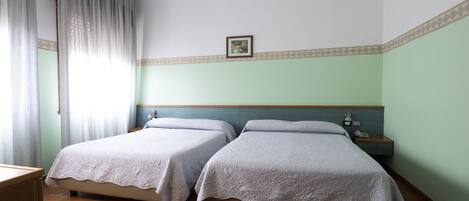 A hotel room with two beds, a nightstand, a framed picture on the wall, and a window with curtains.