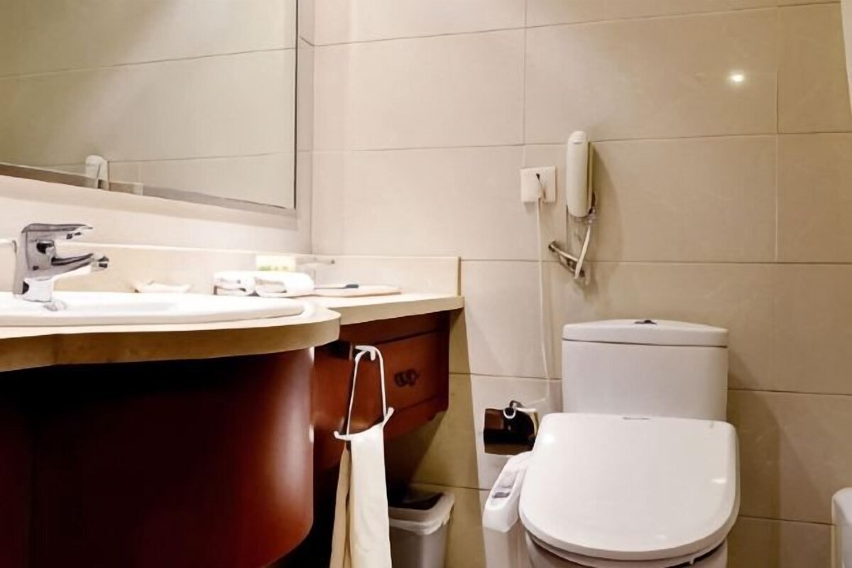 A bathroom with a sink, mirror, toilet, and a trash bin.
