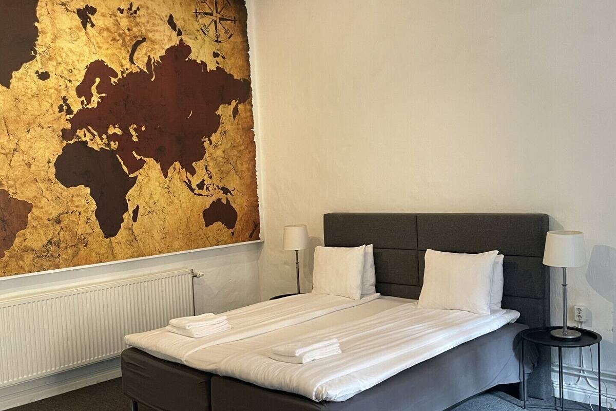 A modern hotel room with a large world map mural, a large bed, two bedside tables, and a radiator.