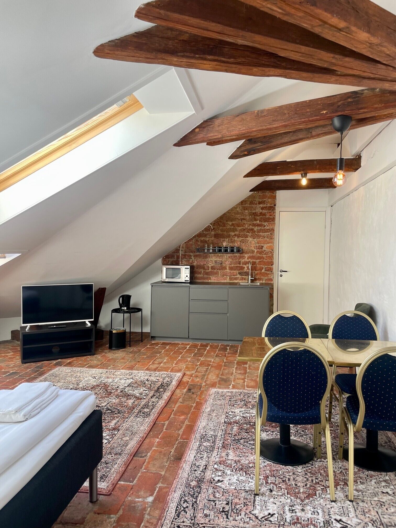 Un dormitorio estilo loft con techo inclinado, televisión, cama y zona de comedor con sillas y mesa.