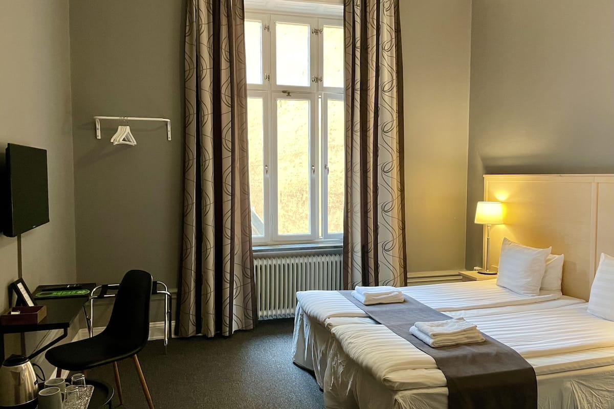 A hotel room with two beds, a desk with a chair, a TV, and a window with curtains.