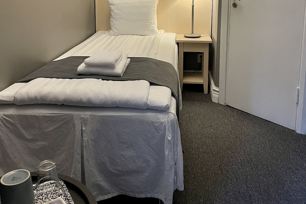 A hotel room with a neatly made bed, a bedside lamp, a door, and a small table with a tray.