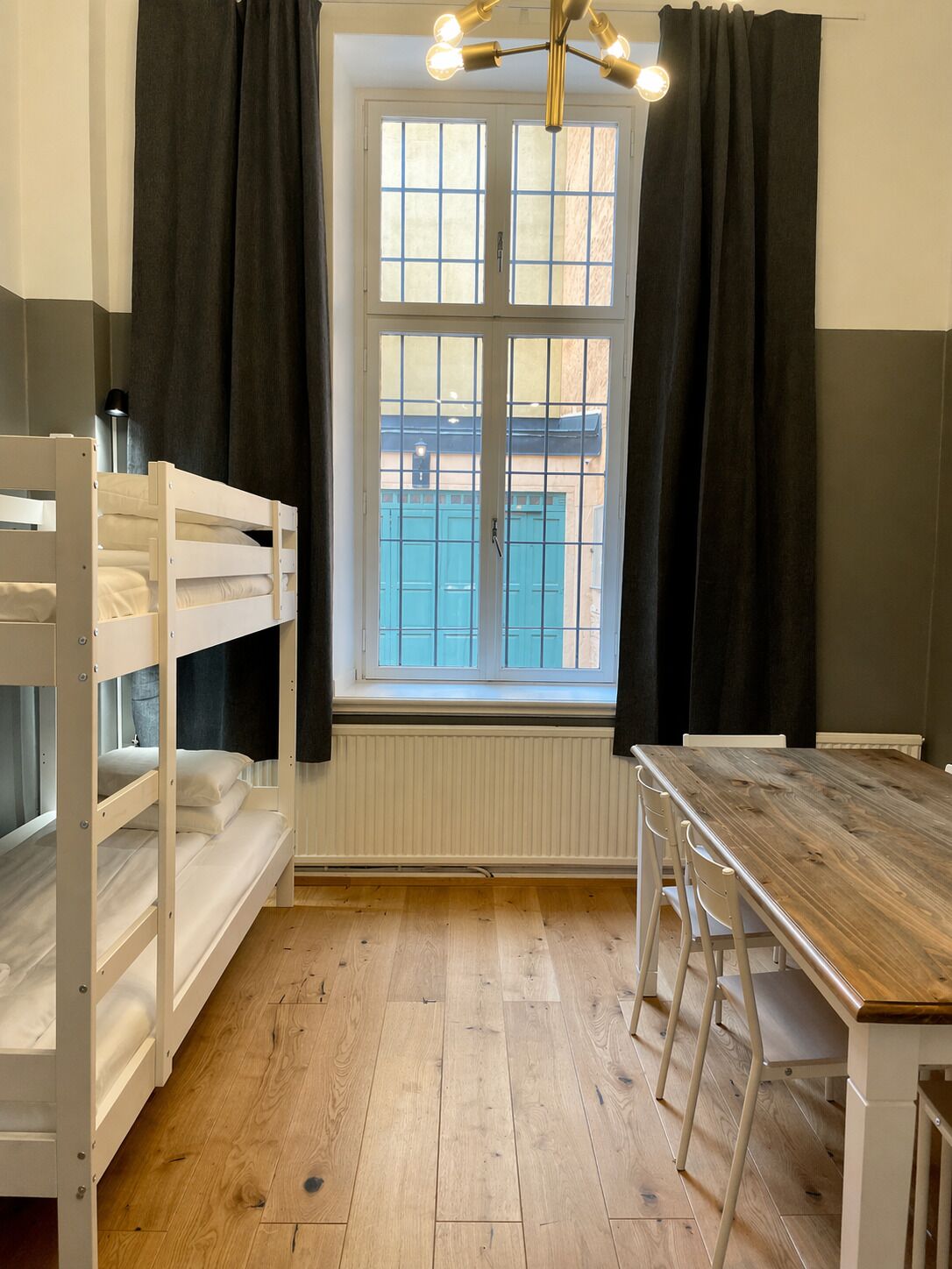 Una habitación con literas, una mesa de madera y una ventana con cortinas.